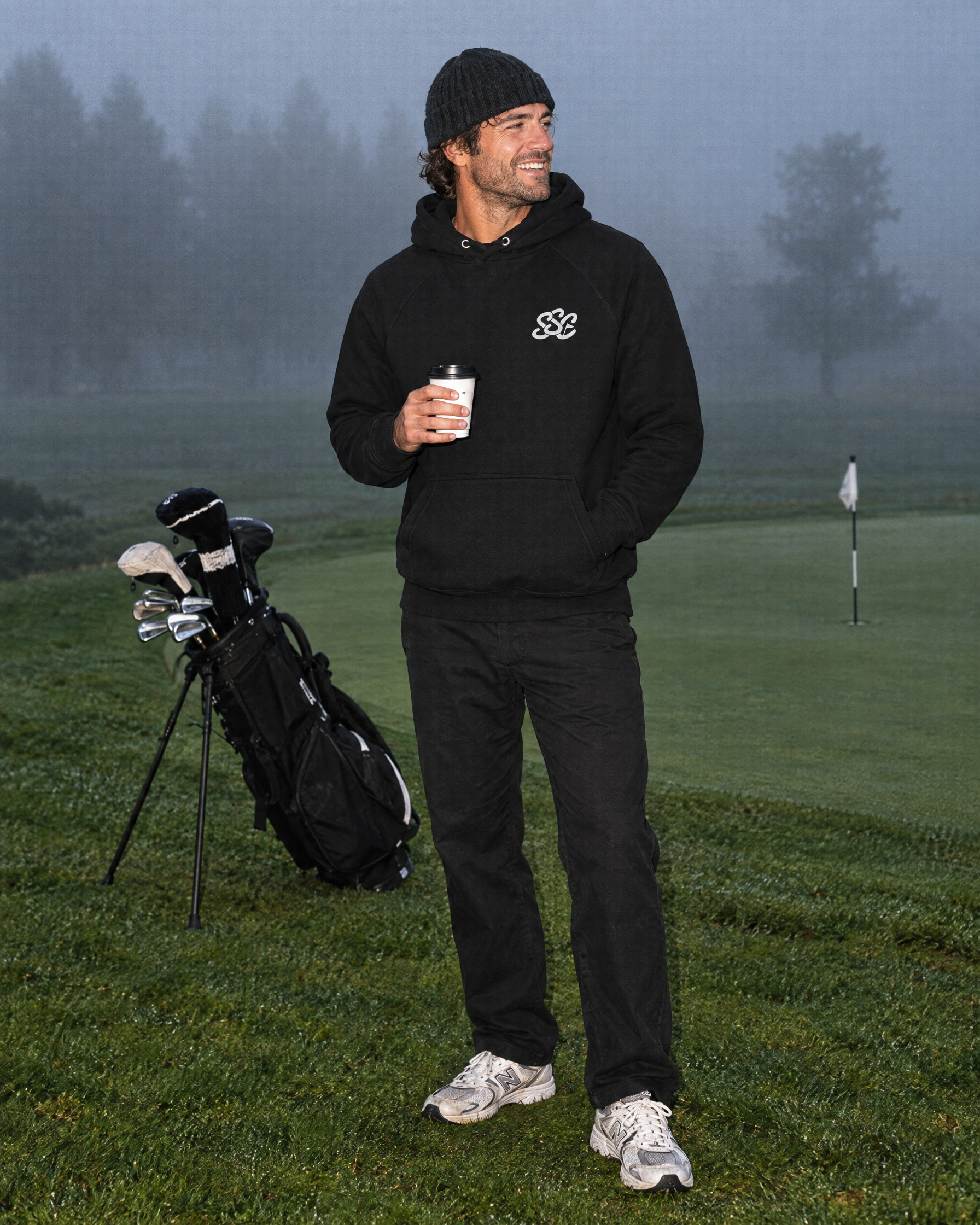 Sunday Classic Hoodie in Black with coffee at the misty putting green | Sunday Swing Club